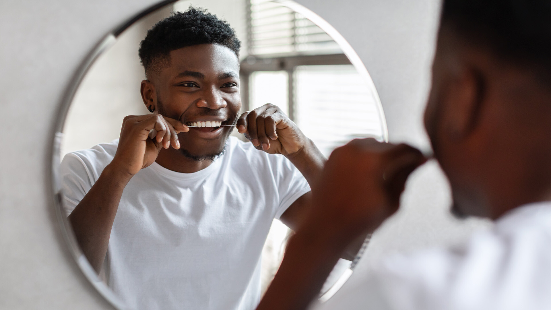 Photo of a man flossing his teeth in the mirror