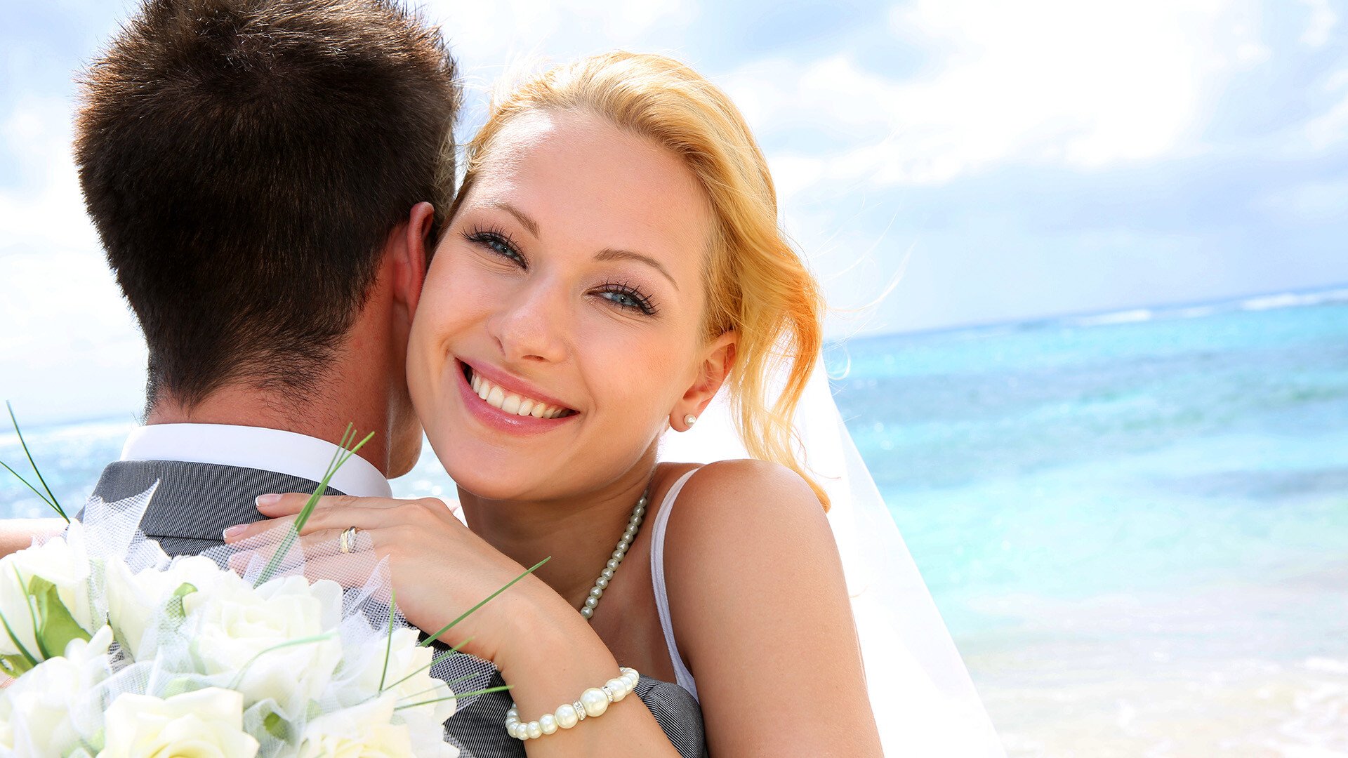 Close up shot of a bride hugging the groom and smiling at the camera with very white teeth