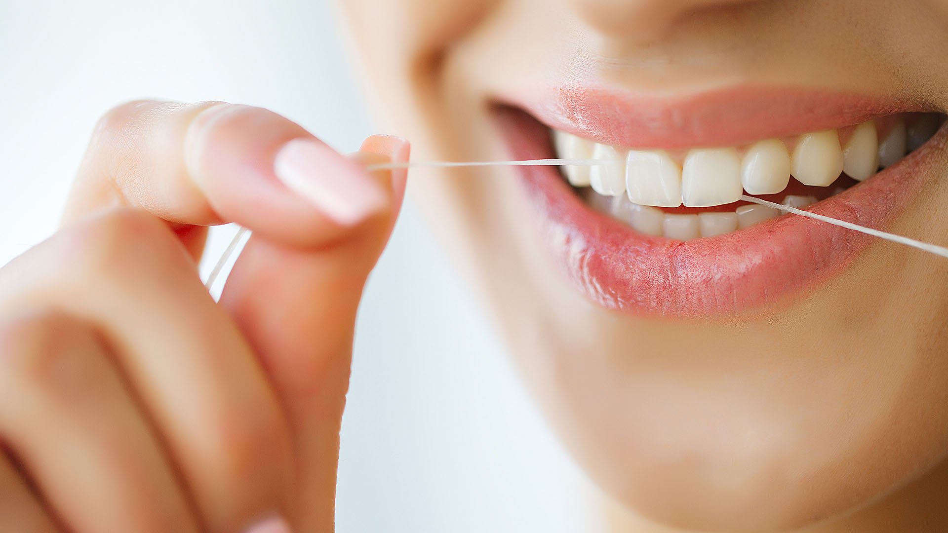 Close up shot of a woman using floss while smiling 