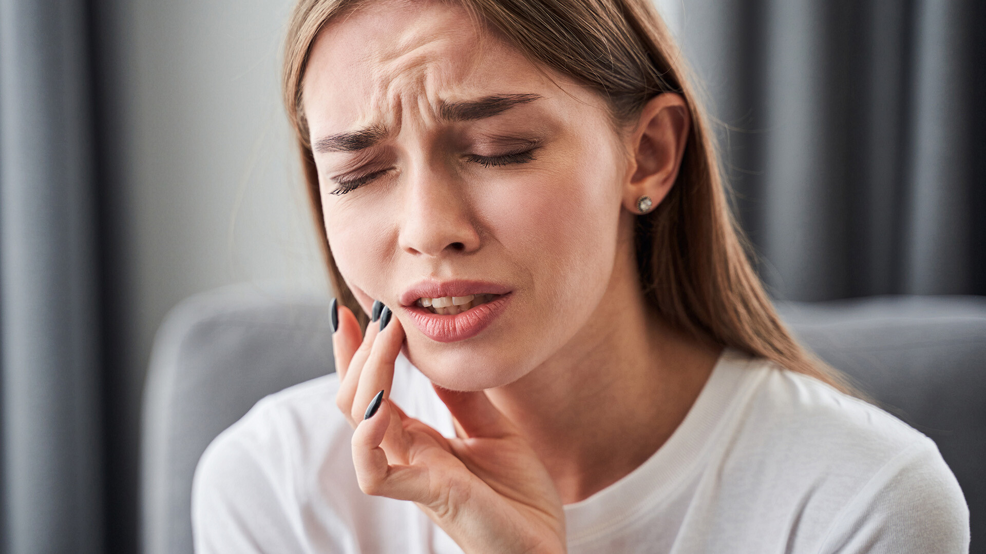 Close up shot of a woman holding her cheek with her fingers who looks to be in pain from something in her mouth