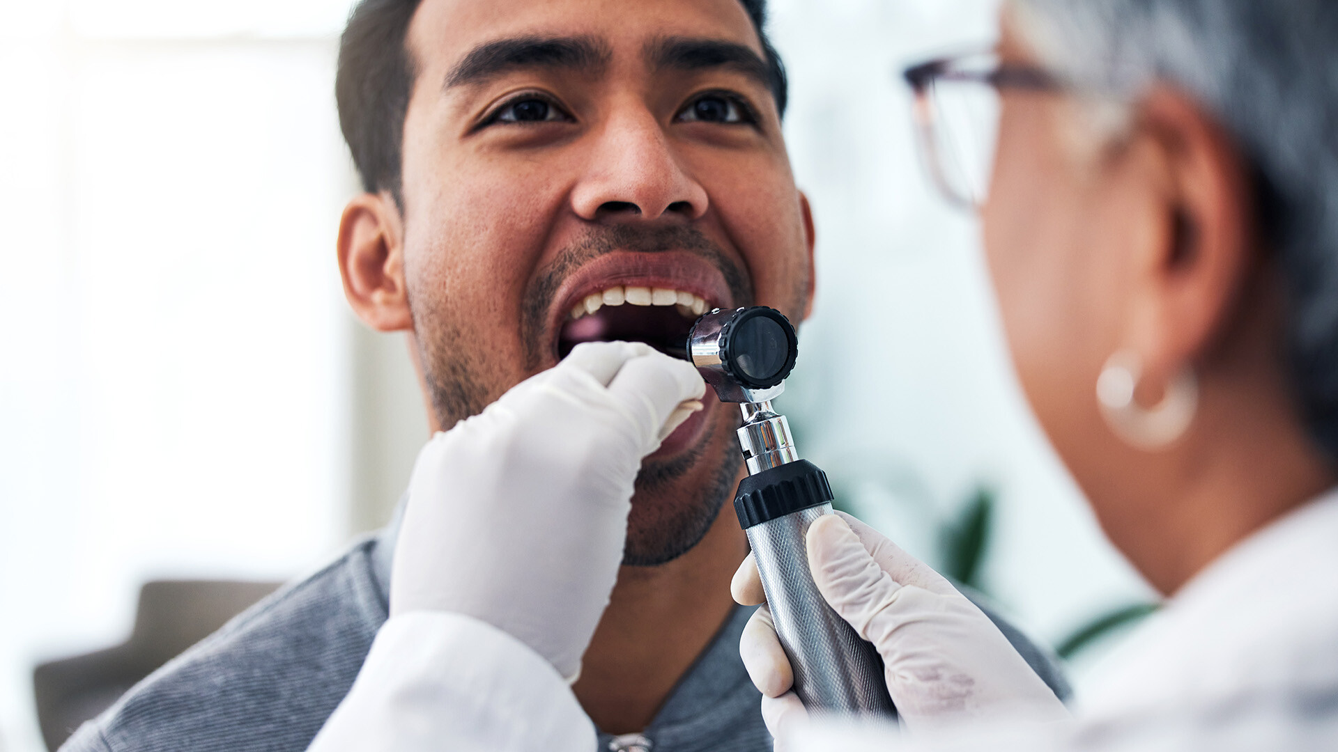 Image of a doctor in gloves examining the mouth of a patient 