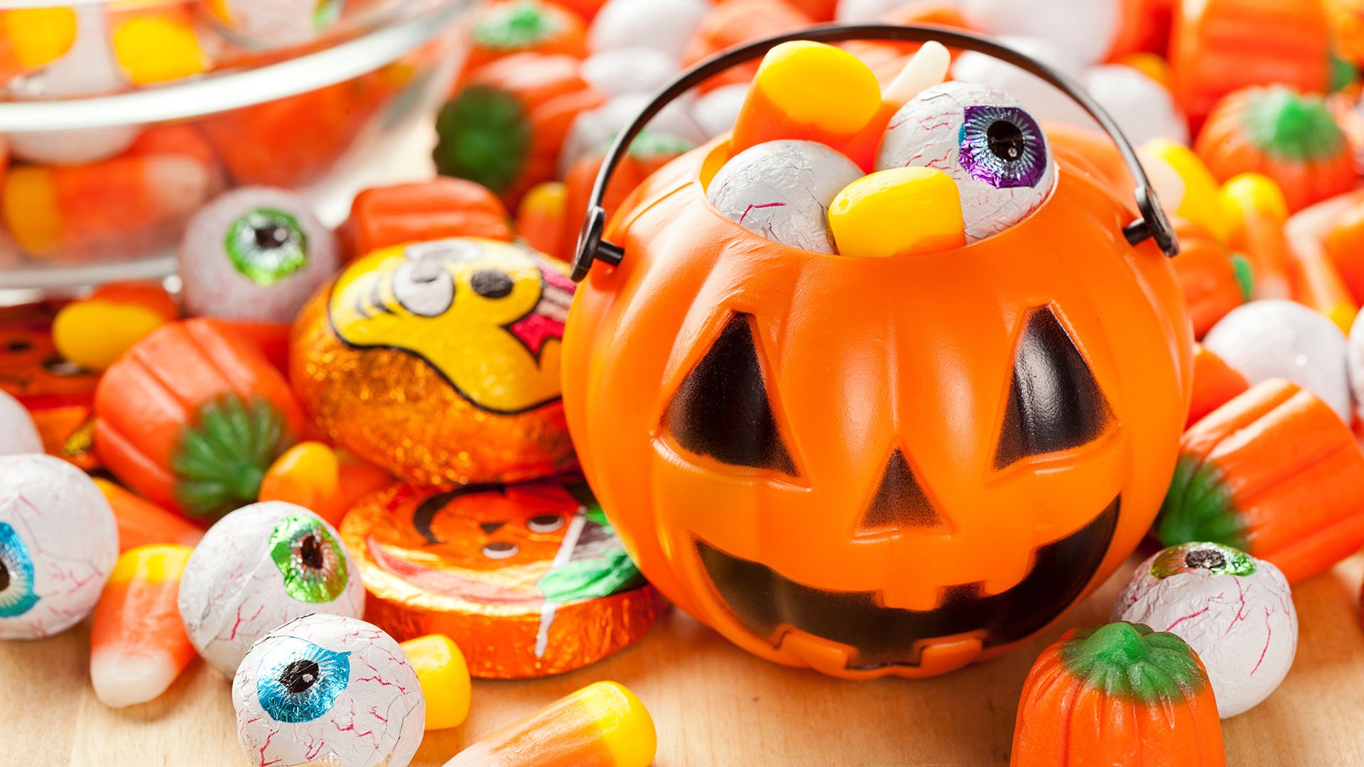 Close up image of a different variety of Halloween candy along with a pumpkin shaped bucket for carrying candy