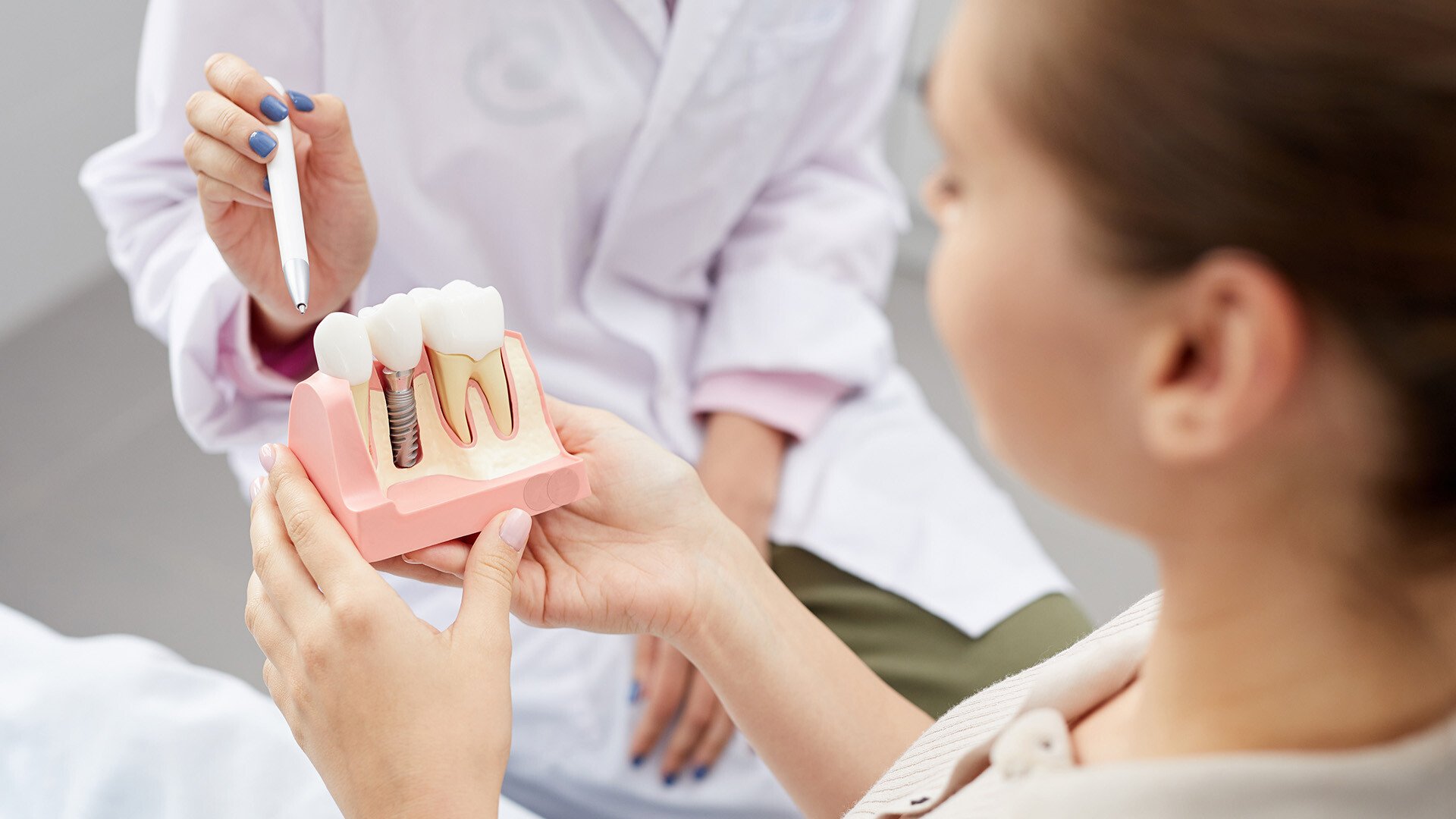 Female doctor holding a pen and pointing to a tooth model that a patient is holding which shows different implant options